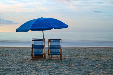 Two beach chairs and umbrella by the seashore; long exposure.