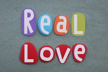 Real love, creative slogan composed with multi colored hand painted stone letters over green sand