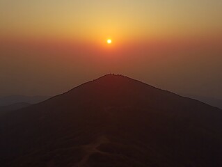 A vibrant sunset illuminates a mountain landscape with a distant peak