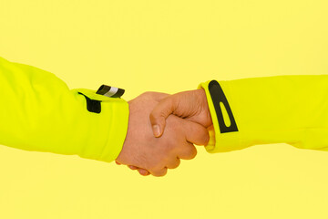 Two individuals in bright yellow jackets shaking hands against a vibrant yellow background,...