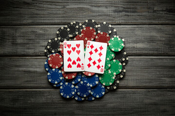 Colorful poker chips surround a pair of playing cards on a rustic wooden table, capturing the thrill of a game night with friends