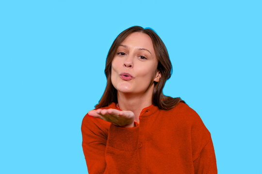 Woman blowing kiss against bright blue background while wearing  cozy red sweater