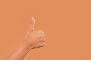 Hand giving a thumbs up against a plain orange background, symbolizing approval or positivity in a...