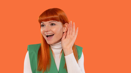Bright orange backdrop enhances the cheerful expression of a young woman as she playfully cups her...