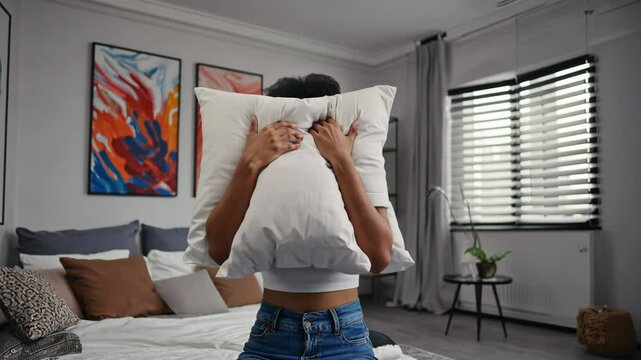 A young man buries his face into a pillow, overwhelmed by stress, insomnia, or nightmares. The soft lighting and emotional body language make this ideal for mental health, anxiety