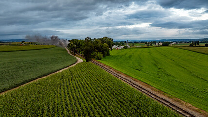 Steam Train Travels Through Lush Farmland Under a Cloudy Sky in the Countryside