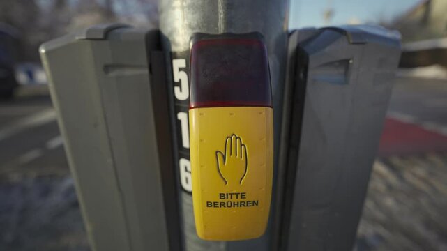 Pedestrian crossing button in Munich, Germany in winter. The yellow tactile button reads Bitte beruehren and Signal kommt providing safety and accessibility for pedestrians in the urban environment. 