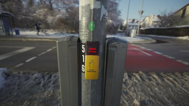 Pedestrian crossing button in Munich, Germany, during winter. Yellow tactile button displays Bitte beruhren. Please touch and Signal kommt. Signal comes, enhancing urban safety and accessibility. 