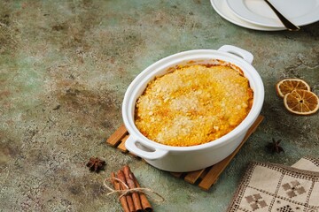 Finnish carrot casserole with rice and crispy crumble on top in white baking dish on green concrete background. Traditional food of Finns at Christmas. Vegetable, vegetarian recipes.