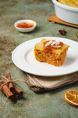 Sliced ​​finnish carrot casserole with rice and crispy crumble on top on white plate on green concrete background. Traditional food of finns at christmas.