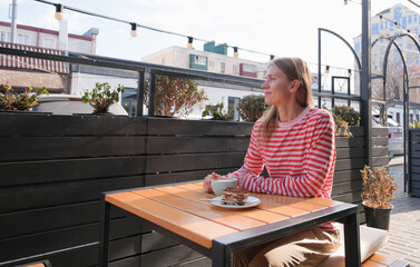 young woman sitting at a street cafe table, sipping coffee and eating dessert