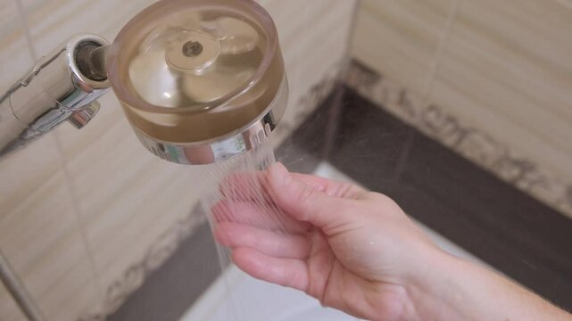 Woman checking temperature of water flowing from shower head with hand in bathroom, top view.