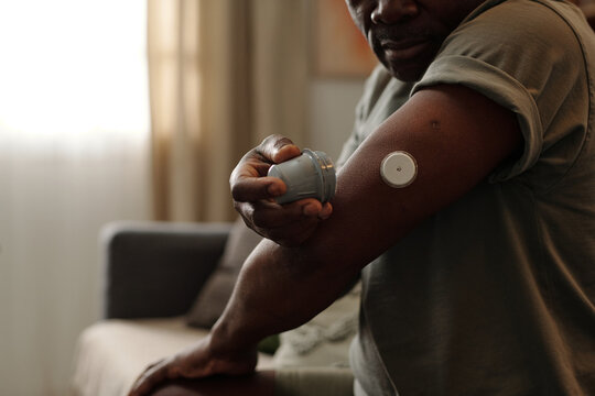 Black person using glucose monitor to check blood sugar levels at home assisted by compact hand-held device for diabetes management
