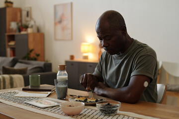 African American man having healthy breakfast at wooden table in minimalistic living room with soft...