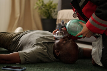 Firefighter providing oxygen to unconscious African American man in living room environment during...