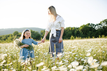 Fototapeta premium Mother playing with child girl 4-5 year old in blooming chamomile meadow wearing casual dresses outdoors. Springtime. Motherhood.