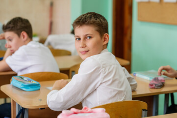 A pupil in class is sitting at a desk in a half-turn, looking at the camera. Education.. School