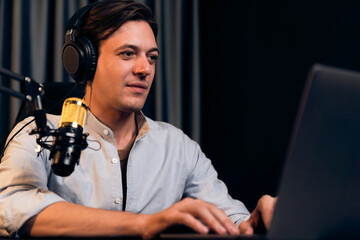 Host channel smart broadcaster talking on live social media application searching on laptop, broadcasting streamer wearing headphone using mic at modern home office studio in warm lighting. Pecuniary.