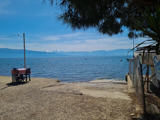 Seaside promenade with a view of the calm blue sea and mountains on the horizon on a sunny day.