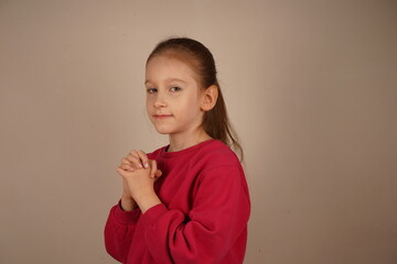 Fototapeta premium A heartfelt portrayal of childhood emotions. The young girl holds her hands locked together in a fist-like gesture, expressing a sense of hope. Her eyes reflect silent anticipation and yearning.