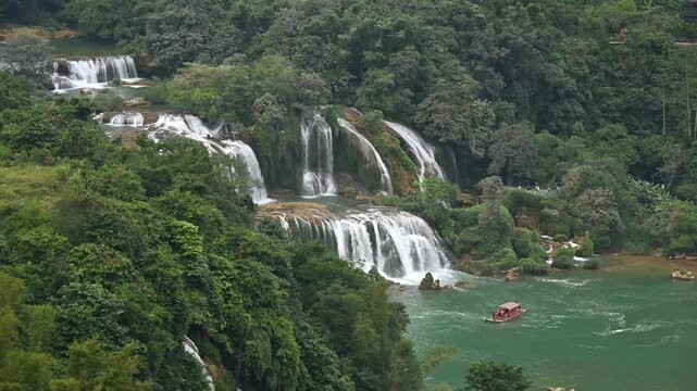 Lush vegetation surrounds the multi tiered Ban Gioc (Detian) Falls, where tourist boats navigate the turquoise waters
