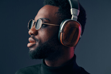Stylish African man wearing sunglasses and headphones, showcasing a modern look and urban vibe in a dark background