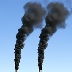 Two smoke stacks emitting dark smoke into the clear sky