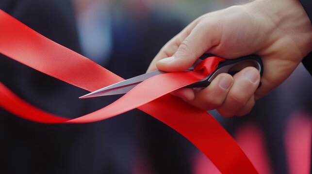 A person is cutting a red ribbon with a pair of scissors to symbolize an official opening or celebration.  