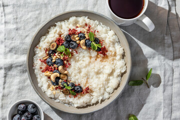 Rice porridge with blueberries, dried raspberries and nuts on a linen tablecloth, hot and healthy breakfast with tea. Bright morning light