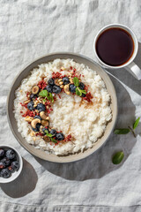 Rice porridge with blueberries, dried raspberries and nuts on a linen tablecloth, hot and healthy breakfast with tea. Bright morning light