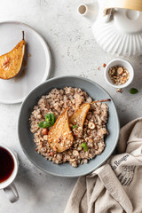 Wholegrain oatmeal porridge with caramelized pear, nuts and honey on white table with tea, healthy food for breakfast