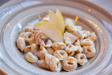 Tortellini Cinque Terre. Close-up shot of a bowl of creamy tortellini pasta garnished with fresh pear slices, showcasing a gourmet meal.