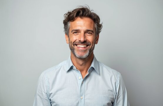Handsome middle aged man portrait. Cheerful guy smiles at camera against gray background. Confident male with beard and grey hair wears casual shirt. Positive emotion, friendly face expression. - Powered by Adobe