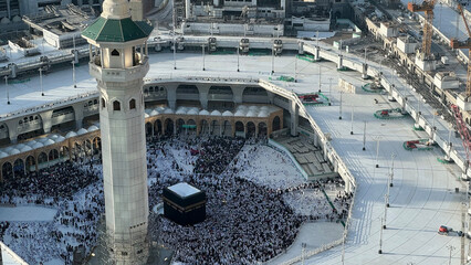 Fototapeta premium Aerial view of Masjid Al-Haram and Makkah city from the Clock Tower, Pilgrims performing Tawaf around the Kaaba during Hajj or Umrah, Magrib pray. The Holy Mosque, Minarets, and skyline highlight this