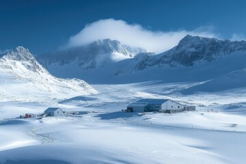 Snowy mountains surround buildings on a flat plain. Blue sky and clouds cover some peaks. Winter landscape shows pristine white snow everywhere.