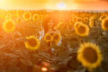 A girl in a hat on a beautiful field of sunflowers against the sky in the evening light of a summer...
