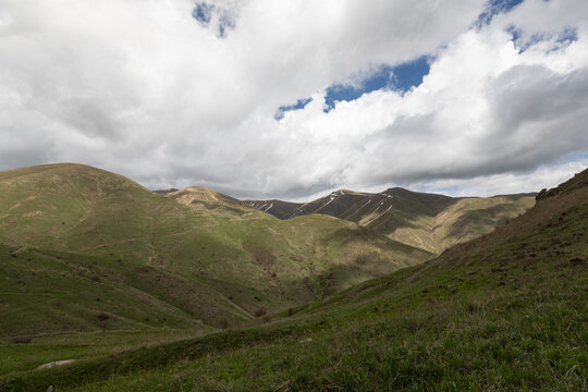 Scenic mountain landscape near Spitakavor Church and Proshaberd Fortress in Vayots Dzor, Armenia. Rolling green hills with patches of snow under a dramatic cloudy sky create a striking view