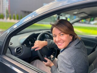 Close up shot of joyful beautiful business lady sitting in own auto and smiling at camera. Positive...