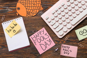 Computer keyboard, notebook and sticky notes on wooden background. April Fools Day prank