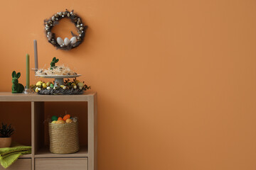 Shelf unit with Easter decor and wreath on orange wall