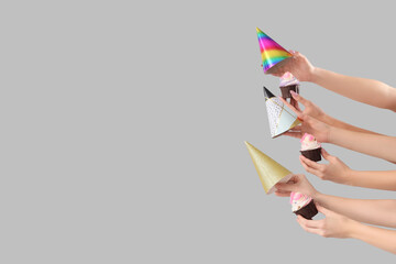 Many female hands with birthday cupcakes and party hats on grey background