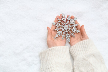 Female hands with beautiful decorative snowflake on snow