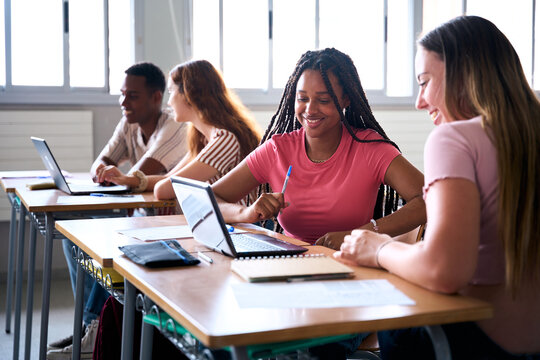Students are studying with computer laptop in classroom. Young people are spending time together. Young caucasian and cheerful African American girl are working together