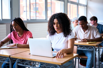 A classroom of multiracial students aged 18 to 20 taking notes during a lecture. In the foreground, a group of African American are focused, highlighting diversity and inclusion in education