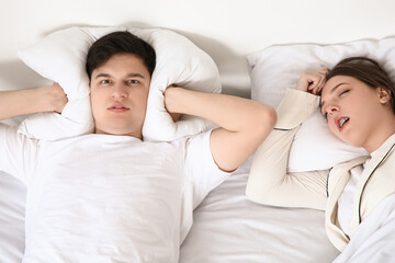 Young annoyed man suffering from loud snoring of his wife at home