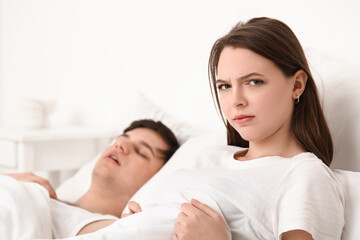 Young annoyed woman lying in bed with her snoring husband at home