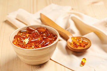 Bowl and spoon with fish oil capsules on wooden table