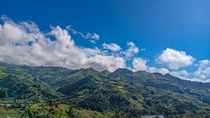 Stunning views of lush green mountains under a bright blue sky with scattered white clouds,...