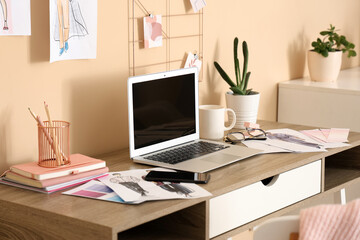 Blank laptop with cup and plant on fashion designer's table in office