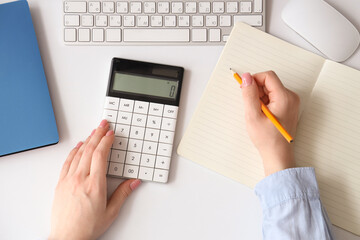 Female accountant with calculator, computer mouse, keyboard and notebooks at table in office